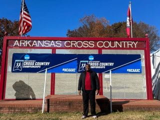 Alexander Mitchell stands in front of UARK Cross Country Sign.